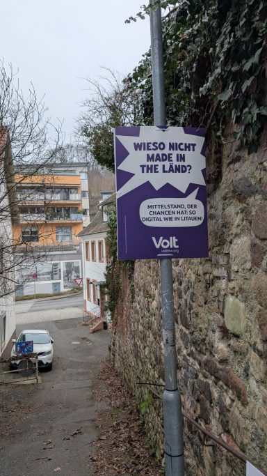 Schild mit der Aufschrift "WIESO NICHT MADE IN THE LÄND?" in einer schmalen Gasse.