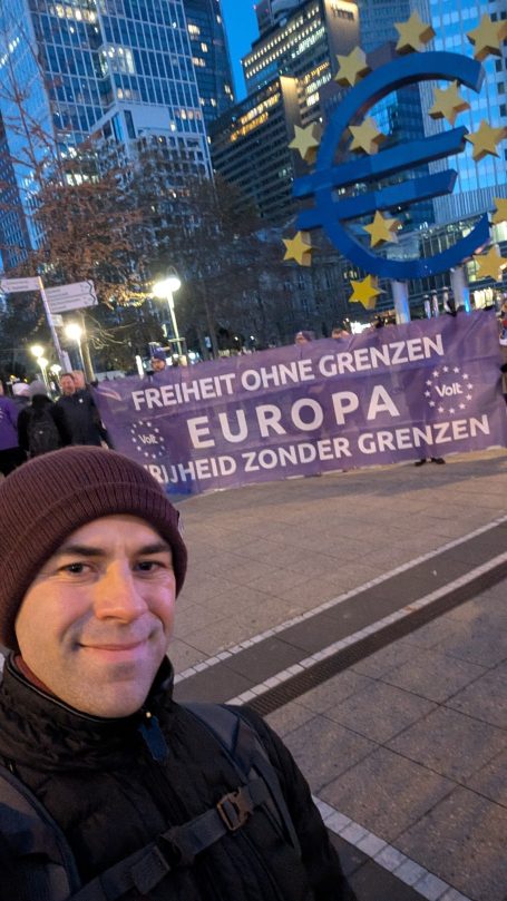 Person mit Mütze vor einem großen Euro-Zeichen und einem Banner für Europa.